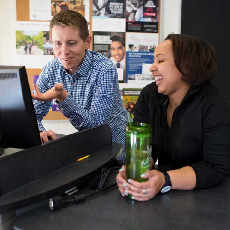 Two staff members converse while looking at a computer screen. 